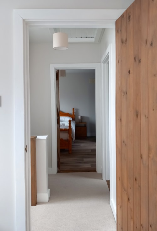 Hallway at Leitrim Quay cottage with wooden doors, white walls, pendant light, and view of bedroom with wooden furniture