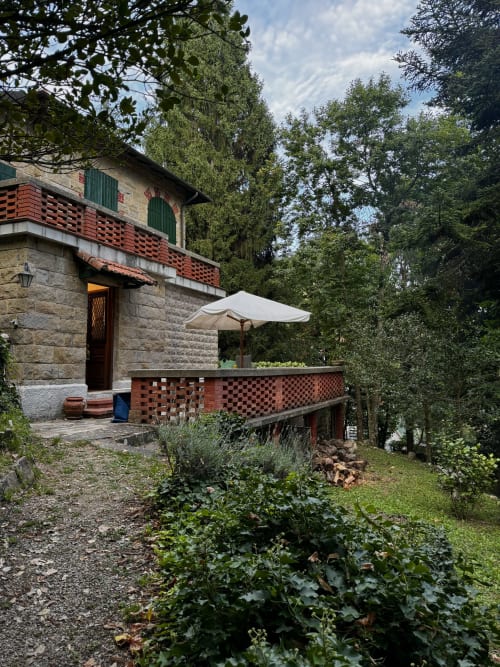 Vista del giardino di Villa Vittoria a Sanremo con patio in terracotta, ombrellone bianco e rigogliosa vegetazione intorno all'edificio in pietra