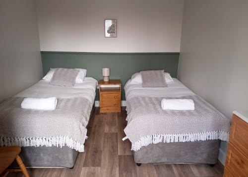 Twin bedroom at Leitrim Quay cottage with two single beds, wooden bedside table, and sage green headboard feature wall