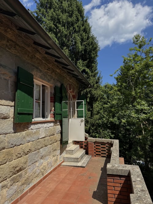 Ingresso di villa in pietra con persiane verdi e porta in legno, immerso nel giardino di Sanremo circondato da edera e alberi
