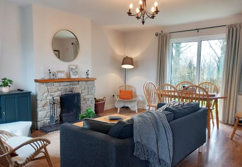 Spacious living room at Leitrim Quay cottage with fireplace, dining table, dark sofa, wooden chairs, and large windows