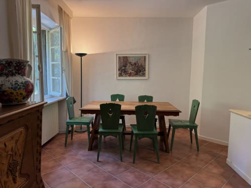 Sala da pranzo con tavolo in legno, sedie verdi, piastrelle in cotto e vista sul giardino a Villa Vittoria, Sanremo