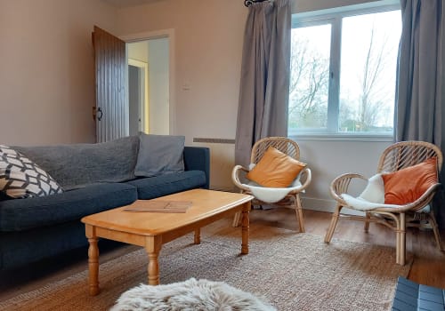Cozy living room in Leitrim Quay cottage with blue sofa, wooden coffee table, rattan chairs with orange cushions, and lake