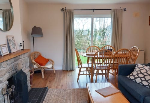 Leitrim Quay cottage living room with fireplace, wooden dining table, chairs, sofa, and garden views