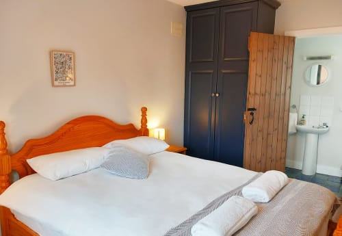 Bright bedroom at Leitrim Quay cottage with wooden bed, white linens, dark wardrobe, and en-suite bathroom visible