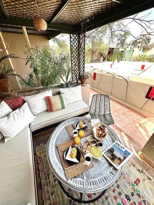 Terrasse de la villa Riad 191 à Marrakech avec petit-déjeuner sur table ronde, mobilier beige, plantes en pots et vue sur la piscine