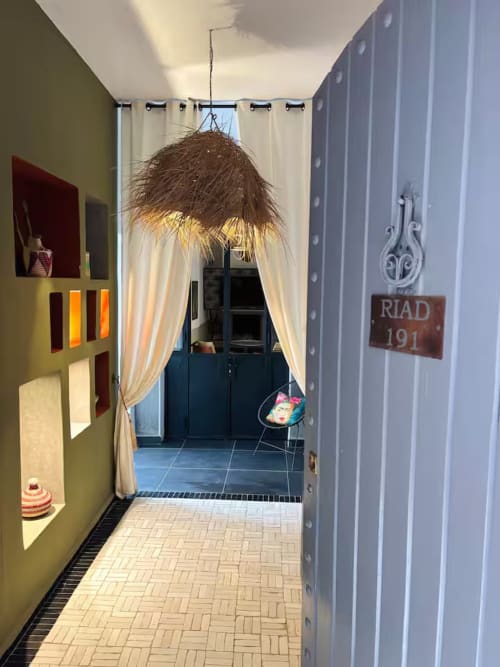 Entrée du riad 191 à Marrakech : murs vert olive, rideaux crème et suspension décorative au-dessus de la porte