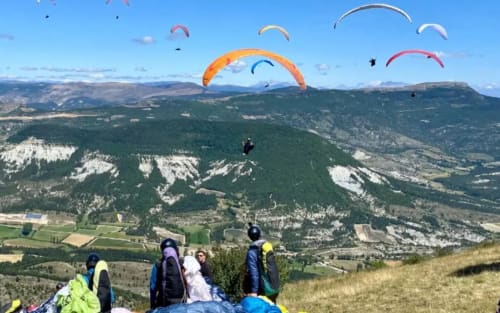 Parapentistes décollant d'une colline surplombant la vallée de Barret-sur-Méouge avec montagnes boisées et terres agricoles en contrebas