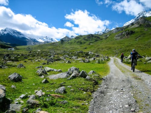 Vététistes sur sentier de gravel dans une prairie alpine avec pics enneigés près de Barret-sur-Méouge
