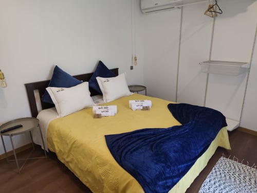Quarto Bungalow Deluxe da Quinta Salinas com colcha amarela, almofadas azul-marinho, roupa de cama branca e vista para piscina em Aveiro