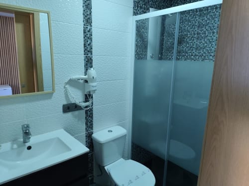 Casa de banho moderna do Hotel Quinta Salinas em Aveiro com azulejos brancos, detalhes em mosaico escuro, box de duche, sanita e lavatório