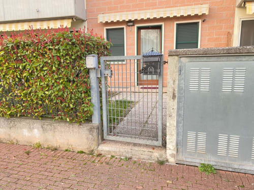 Ingresso con vista sul giardino dell'appartamento Le case di Clara, con edificio in mattoni rossi, cancello in ferro e rigogliosa edera