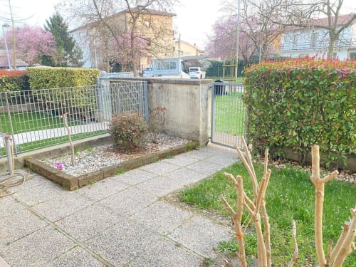 Vista del giardino dell'appartamento Le case di Clara con patio pavimentato, arbusti in fiore e alberi fioriti in primavera