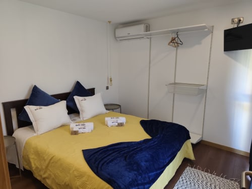 Quarto da pousada Quinta Salinas com cama amarela, almofadas azul-marinho, ar condicionado, guarda-roupa, TV de tela plana e piso em madeira