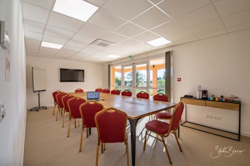 Salle de conférence moderne de l'Hôtel Moulin de la Roque à Althen-des-Paluds avec chaises rouges, table en bois et portes vitrées