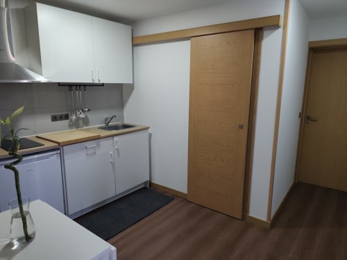 Cozinha compacta no Bungalow Deluxe Quinta Salinas com armários brancos, bancadas de madeira e porta de correr em madeira para
