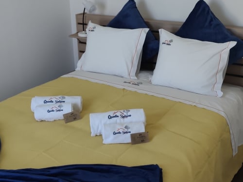 Cama de bungalow da Quinta Salinas com colcha amarela, almofadas brancas, almofadas azul-marinho e toalhas enroladas em Aveiro