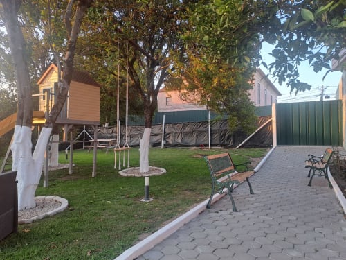 Pátio ajardinado da Quinta Salinas com bungalow, bancos, árvores frondosas e gramado em Aveiro