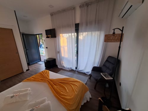 Quarto moderno do bungalow em Quinta Salinas Aveiro com manta laranja, portas de pátio com vista para jardim, TV e área de estar