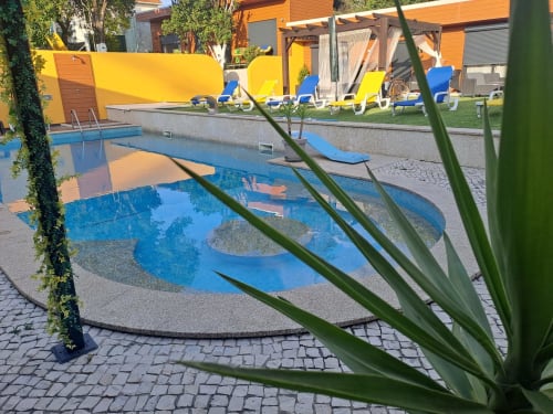 Piscina ao ar livre com água azul no hotel Quinta Salinas em Aveiro, cercada por espreguiçadeiras e pérgulas amarelas