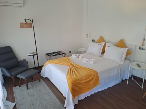 Quarto luminoso do hotel Quinta Salinas em Aveiro com cama queen, detalhes amarelos, poltrona preta e vista para o jardim