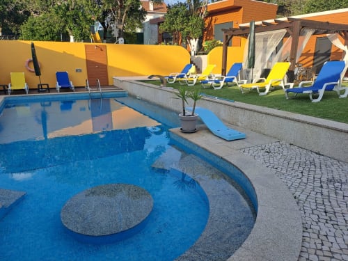Piscina do hotel Quinta Salinas em Aveiro com água azul, espreguiçadeiras coloridas, guarda-sóis amarelos e área de gramado verde