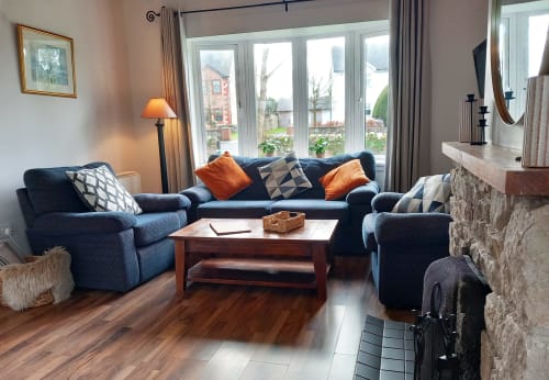 Cozy cottage sitting area with navy blue sofa, orange accents, wood table, fireplace, and lake views at Leitrim Quay