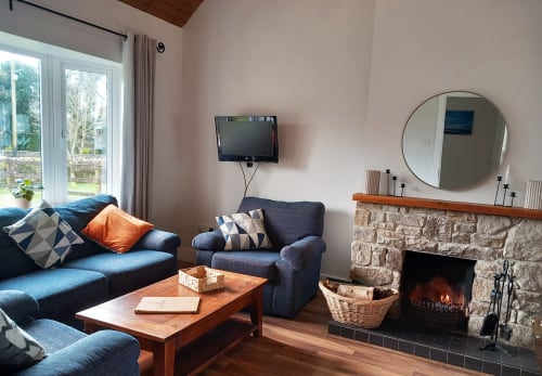 Cozy cottage sitting area with blue sofa, fireplace, lake views, and wood furnishings at Leitrim Quay.