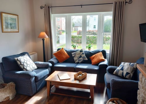 Spacious sitting area in Leitrim Quay cottage with blue seating, orange accents, and lake views through large windows