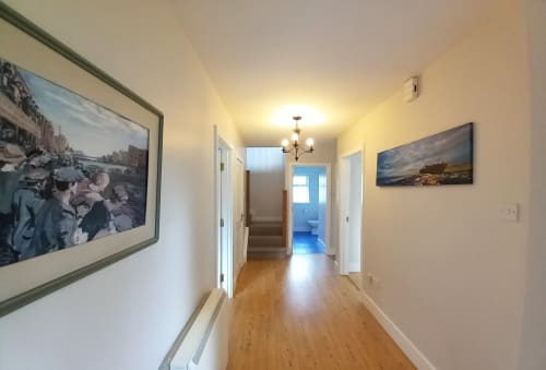 Bright hallway in Leitrim Quay cottage with wooden floors, framed artwork, and open doorways leading to living spaces and