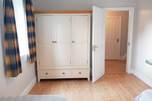 Spacious cottage bedroom at Leitrim Quay with cream wardrobe, wooden floors, plaid curtains, and open doors leading to