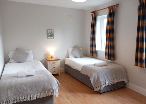 Twin bedroom in Leitrim Quay cottage with two beds, wooden nightstand, striped curtains, and wooden flooring