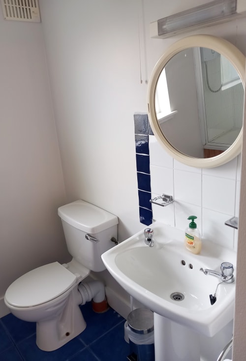 Modern bathroom in Leitrim Quay cottage with white sink, toilet, round mirror, and navy tile accents