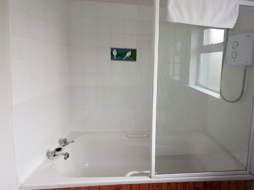 Modern bathroom with bathtub, shower enclosure, and white tiled walls at Leitrim Quay cottage in Ireland