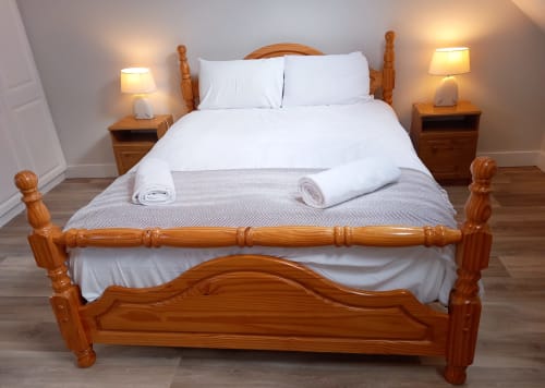 Wooden double bed with white linens and folded towels at Leitrim Quay cottage, bedside lamps and nightstands.
