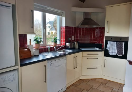 Modern cream kitchen with red tiled backsplash, black countertops, and stainless steel appliances at Leitrim Quay cottage in
