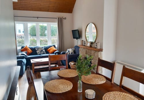 Spacious cottage dining and living area with wooden table, navy sofa, fireplace, and lake views at Leitrim Quay