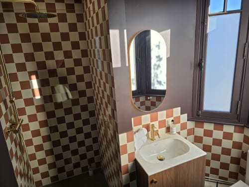 Modern bathroom at Le Castel Bayeux with red and white checkered tiles, oval mirror, white sink, and brass fixtures