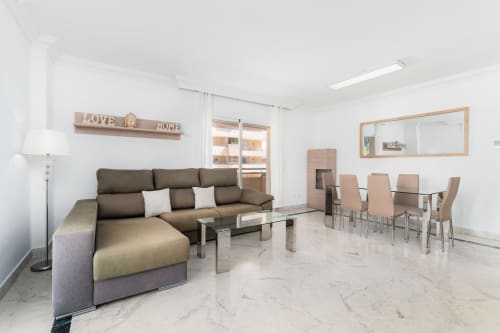Modern living area in Marbella apartment with brown sectional sofa, glass dining table, and marble flooring