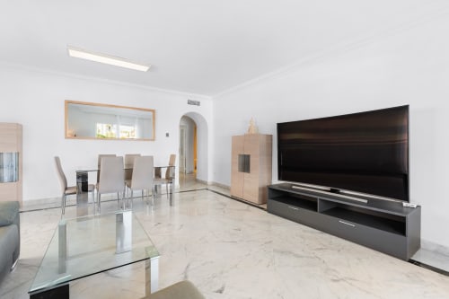 Modern spacious living room in Marbella apartment with large TV, dining area, marble floors, and contemporary furniture