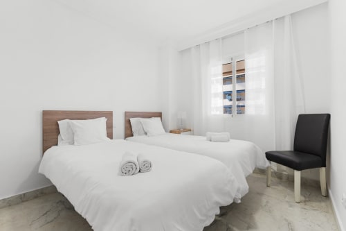 Twin beds with white linens in bright Marbella apartment with city view, modern furnishings and natural light