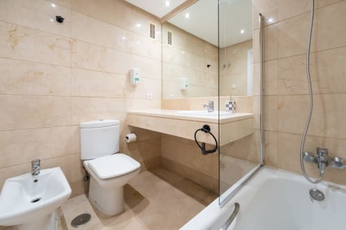 Modern bathroom in Marbella apartment with beige marble tiles, walk-in shower, toilet, and double sink vanity