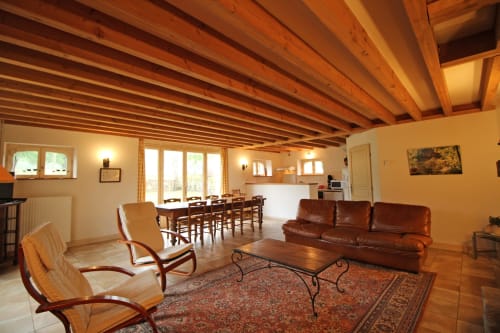 Spacious living room with exposed wooden beams, leather sofa, dining table, and warm lighting in Domaine de Bort gîte