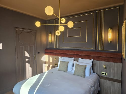Modern bedroom at Le Castel B&B in Bayeux with brass pendant light, geometric wall art, and burgundy upholstered headboard