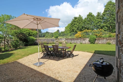 Outdoor patio at Domaine de Bort gîte with dining table, umbrella, and garden views in Saint-Priest-Taurion