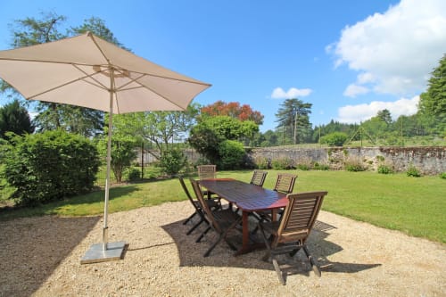 Outdoor dining area with wooden table, chairs, and large umbrella in manicured garden at Domaine de Bort cottage