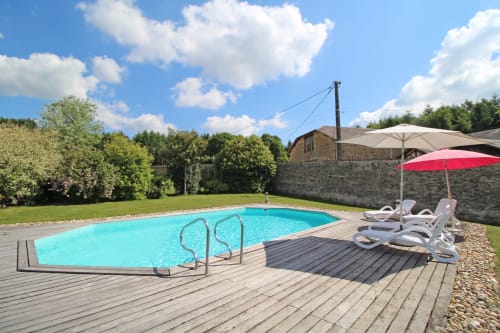 Turquoise swimming pool with deck chairs and red umbrella at Domaine de Bort guesthouse in Saint-Priest-Taurion, France