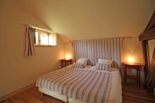 Cozy bedroom at Domaine de Bort gîte in Saint-Priest-Taurion with striped bedding, wooden beams, and warm lighting