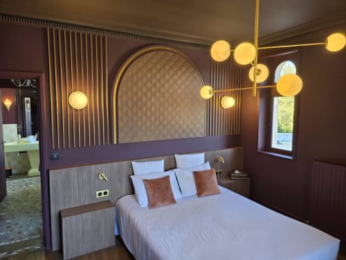Modern hotel bedroom at Le Castel in Bayeux with elegant brass lighting, purple accent walls, and garden views from the