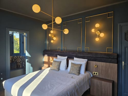 Luxury bedroom at Le Castel Bayeux with modern brass pendant lights, dark headboard, white bedding, and city view balcony